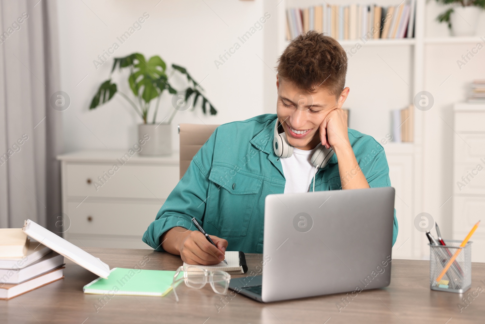 Photo of Student with headphones studying at wooden table indoors