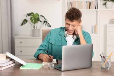 Student with headphones studying at wooden table indoors