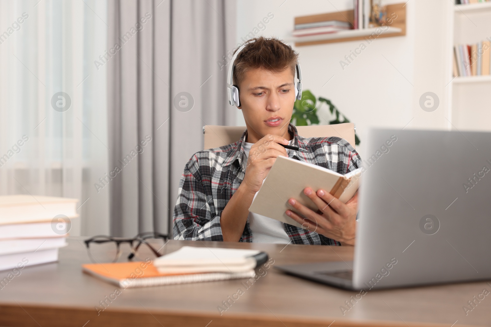 Photo of Student in headphones studying at table indoors