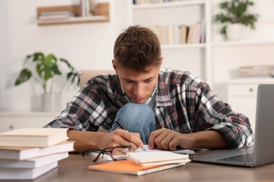 Student taking notes while studying at table indoors