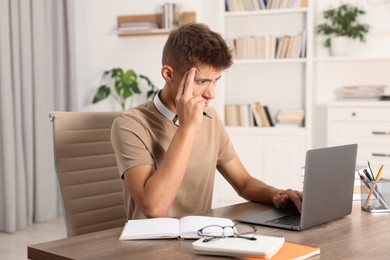 Student studying with laptop at wooden table indoors