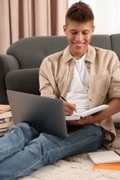 Student taking notes while studying on floor at home