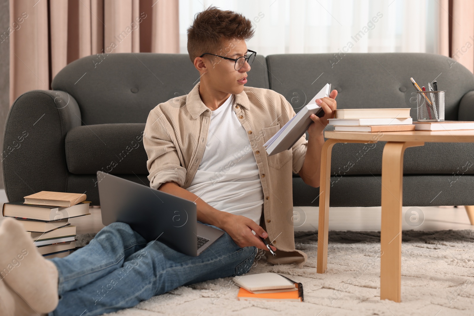 Photo of Student with book and laptop studying on floor at home