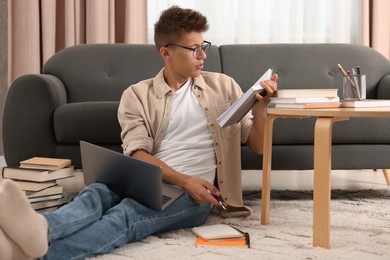 Student with book and laptop studying on floor at home