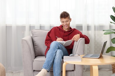 Photo of Student taking notes while studying in armchair at home