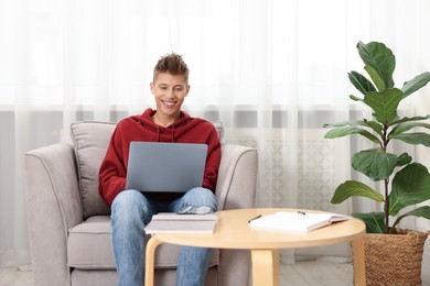 Student studying with laptop in armchair at home