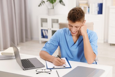 Medical student taking notes while studying at table indoors