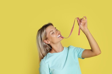 Young woman eating tasty gummy candy on yellow background