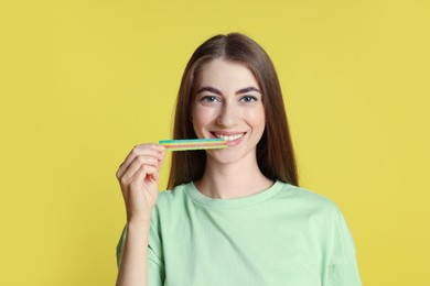 Young woman eating tasty rainbow sour belt on yellow background