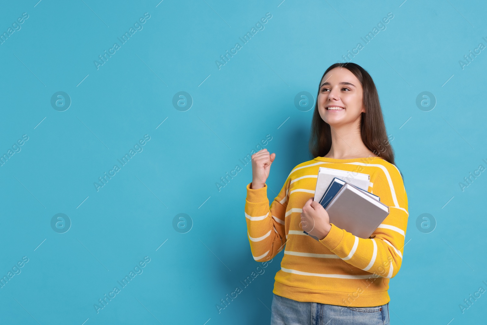 Photo of Young student with books happy about her good exam result on light blue background, space for text