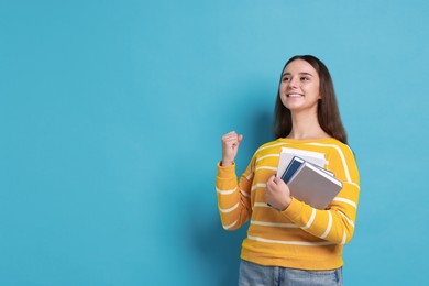 Young student with books happy about her good exam result on light blue background, space for text