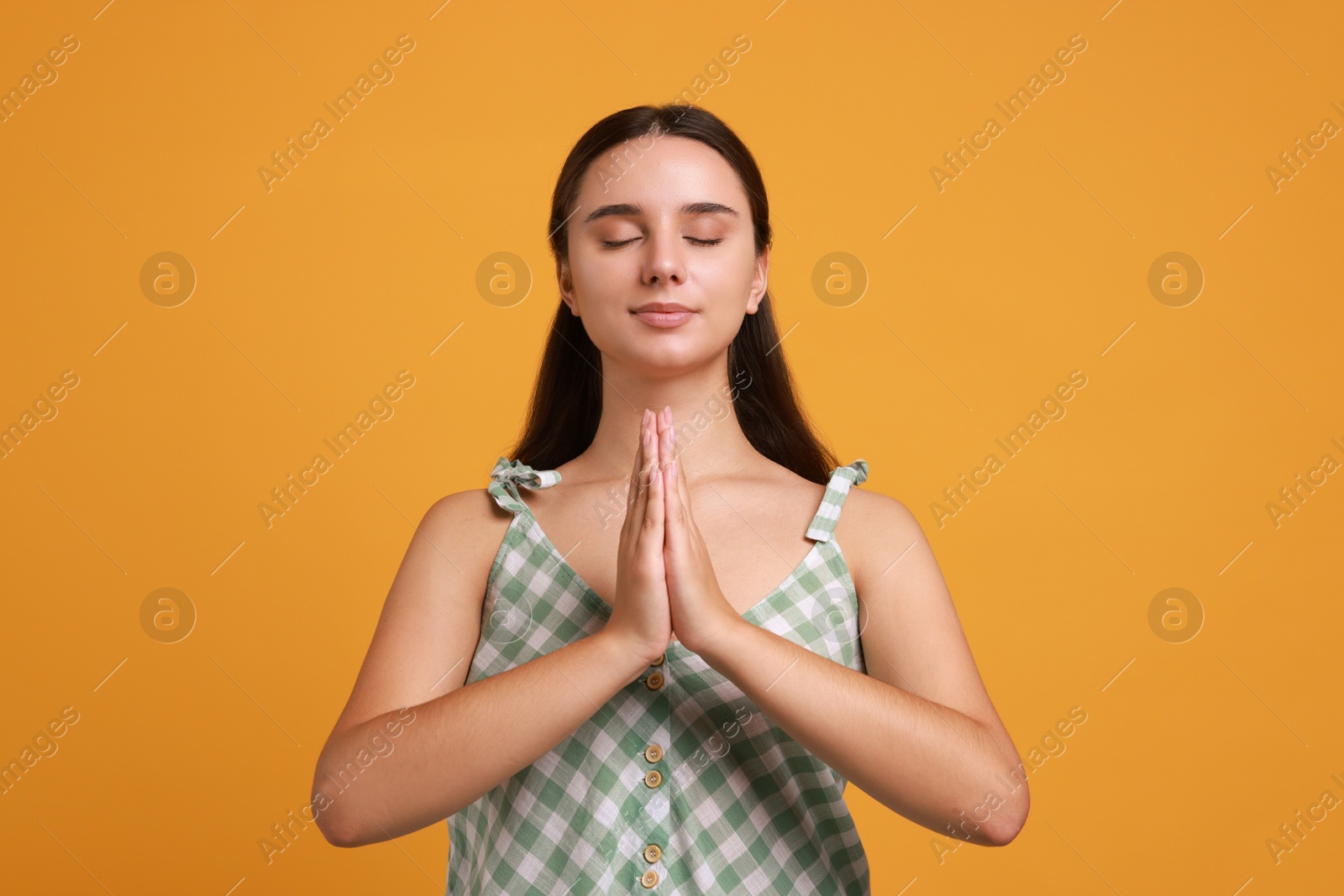 Photo of Young student praying for good exam result on orange background