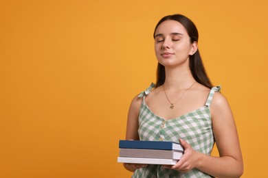 Photo of Young student with stack of books on orange background, space for text