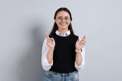 Photo of Excited young student crossing fingers on grey background. Hope for good exam result