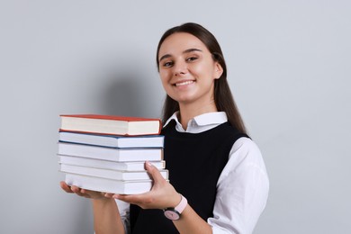 Young student with stack of books happy about her good exam result on grey background