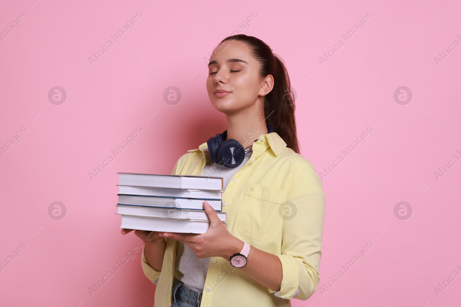 Photo of Young student with stack of books on pink background