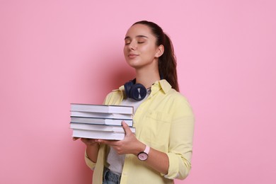 Young student with stack of books on pink background