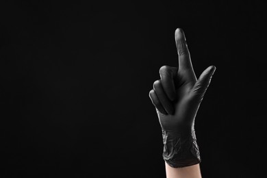 Photo of Man in latex glove pointing at something on black background, closeup. Space for text