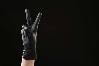 Photo of Man in latex glove showing V-sign on black background, closeup. Space for text