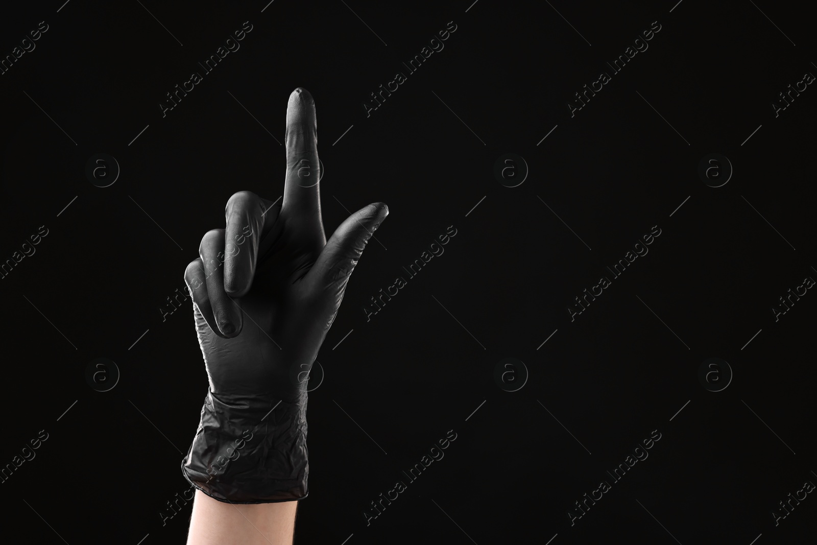 Photo of Man in latex glove pointing at something on black background, closeup. Space for text