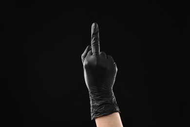 Photo of Man in latex glove showing middle finger on black background, closeup