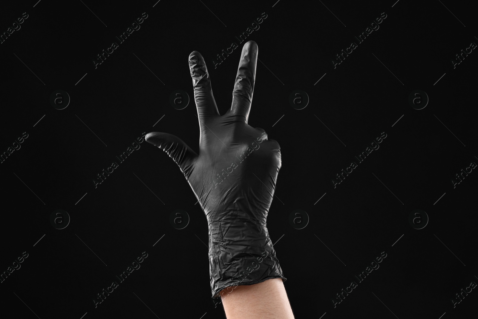 Photo of Man in latex glove showing three fingers on black background, closeup