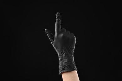 Photo of Man in latex glove pointing at something on black background, closeup