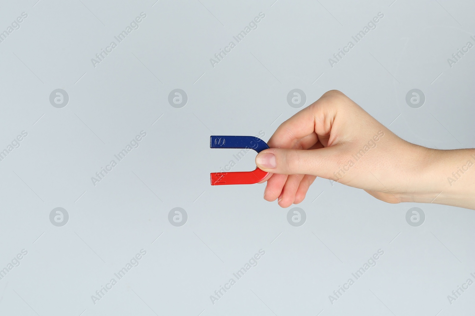 Photo of Woman with horseshoe magnet on grey background, closeup. Space for text