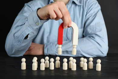 Photo of Man with magnet attracting human figures at black wooden table, closeup