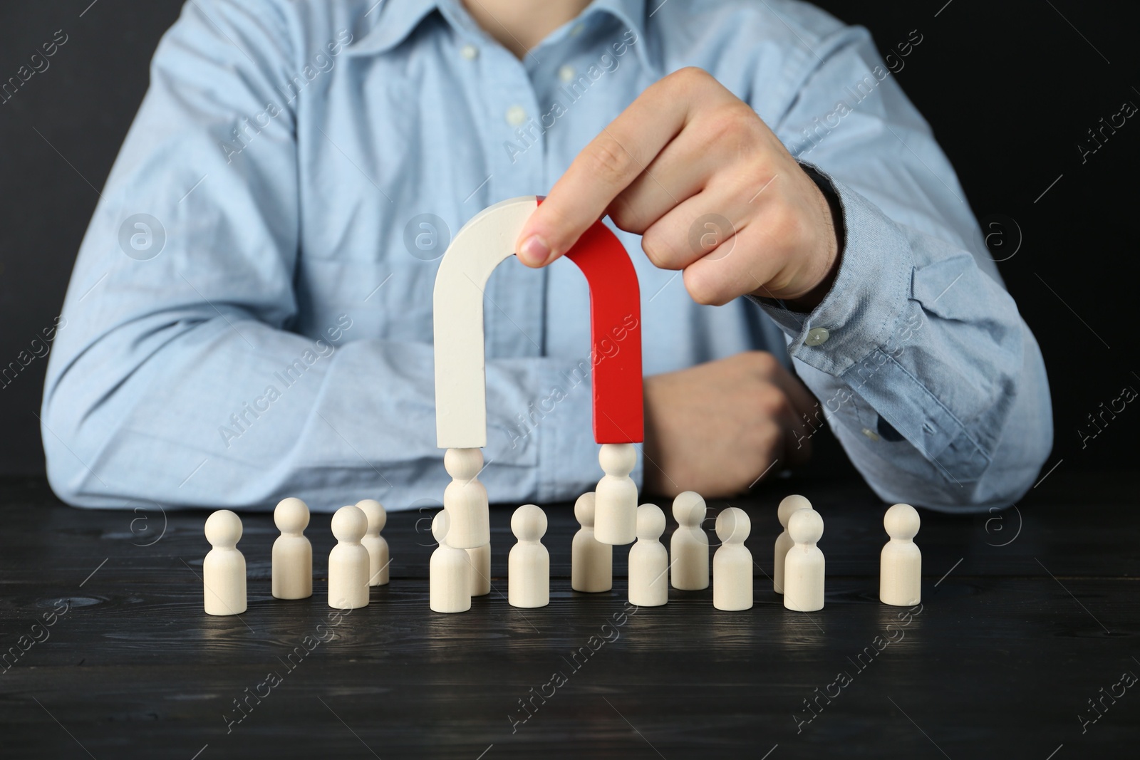 Photo of Man with magnet attracting human figures at black wooden table, closeup