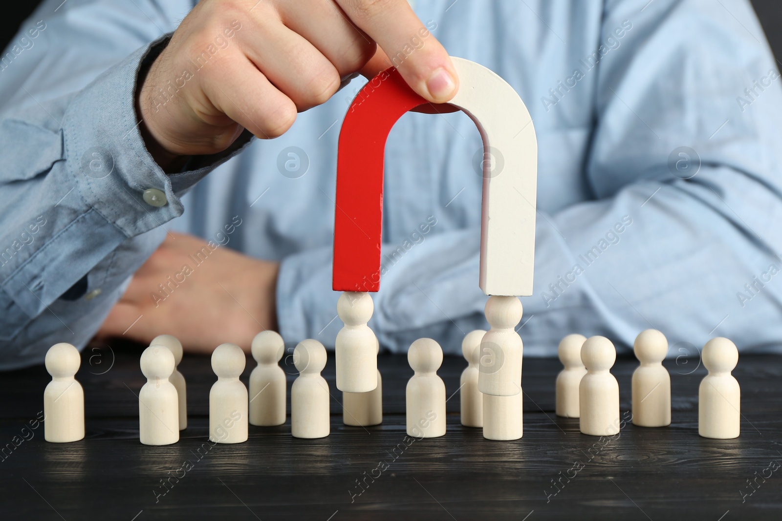 Photo of Man with magnet attracting human figures at black wooden table, closeup