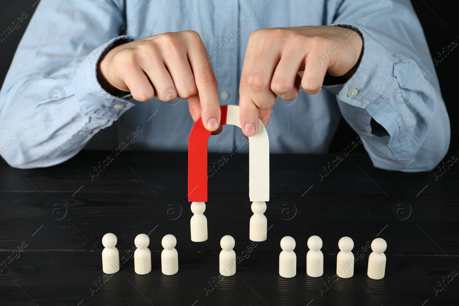 Photo of Man with magnet attracting human figures at black wooden table, closeup