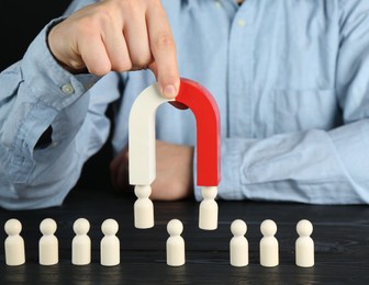 Photo of Man with magnet attracting human figures at black wooden table, closeup