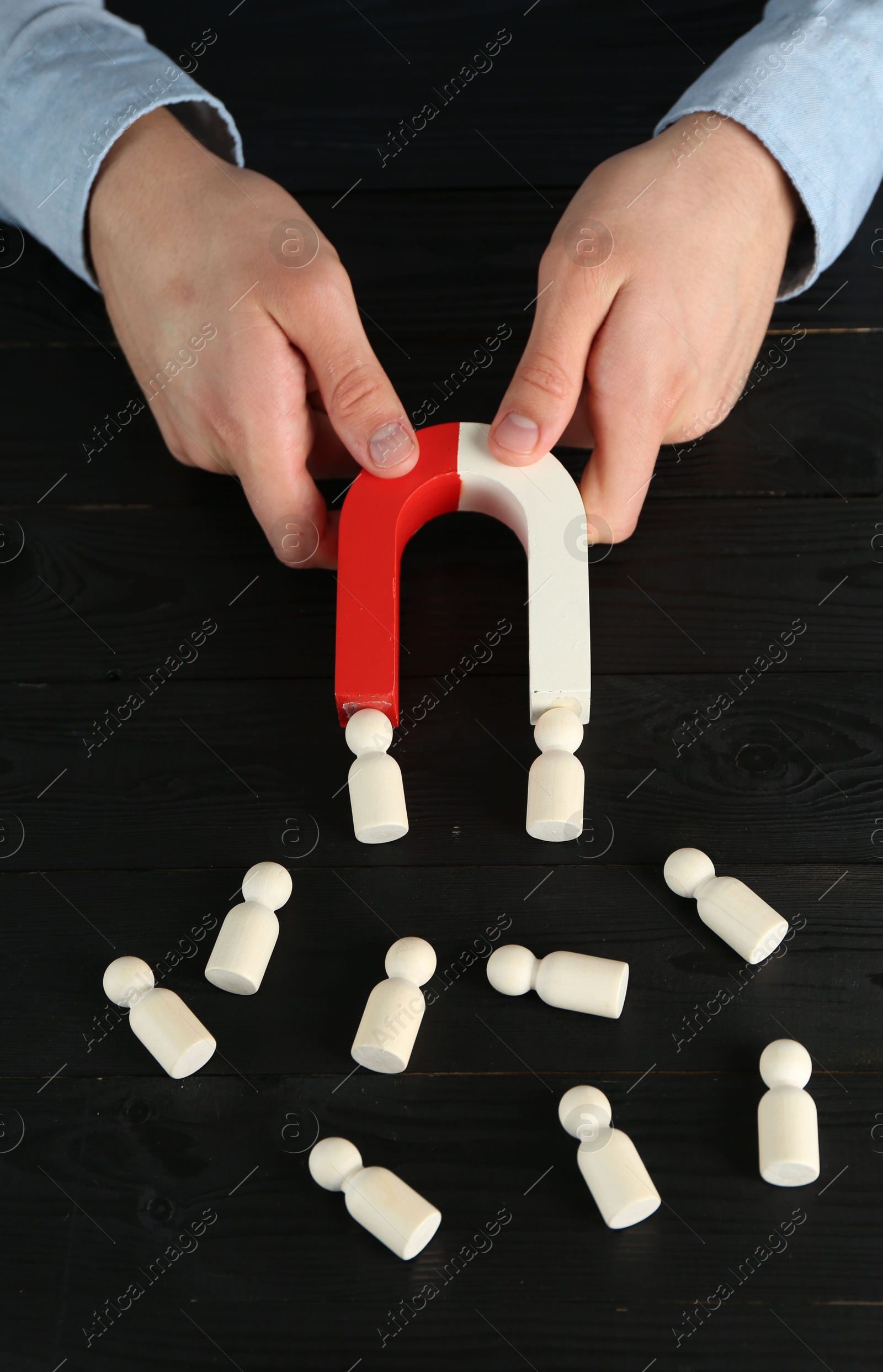 Photo of Man with magnet attracting human figures at black wooden table, closeup