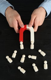 Photo of Man with magnet attracting human figures at black wooden table, closeup