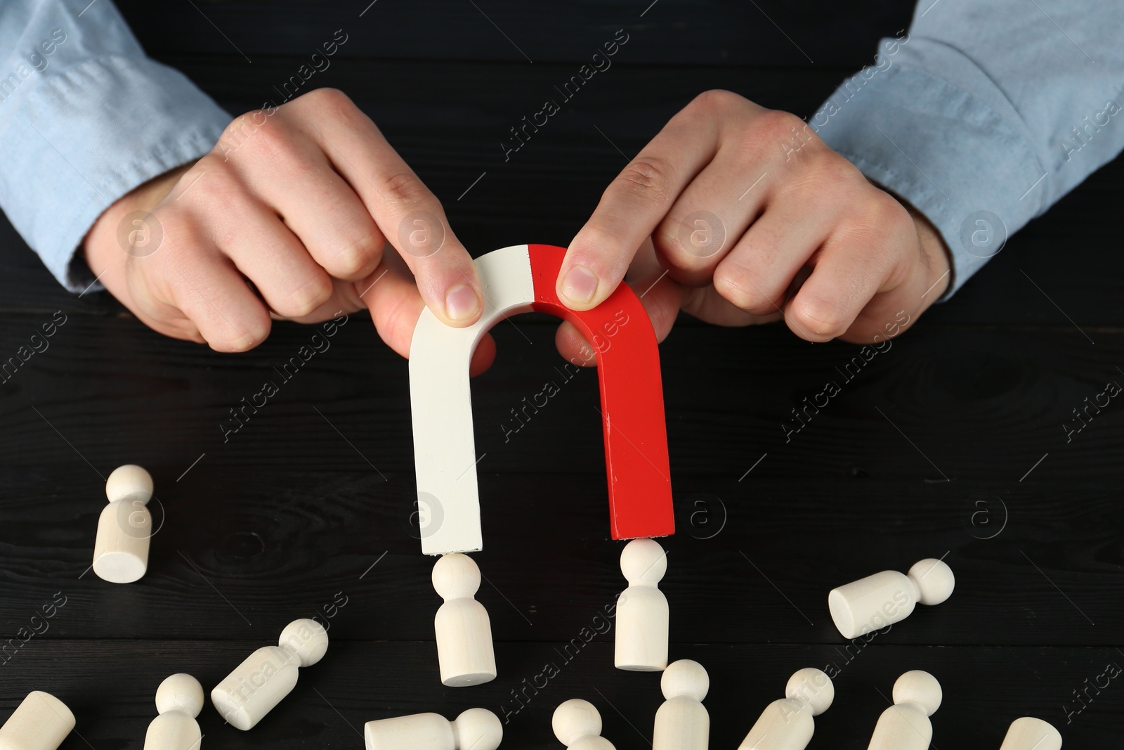 Photo of Man with magnet attracting human figures at black wooden table, closeup