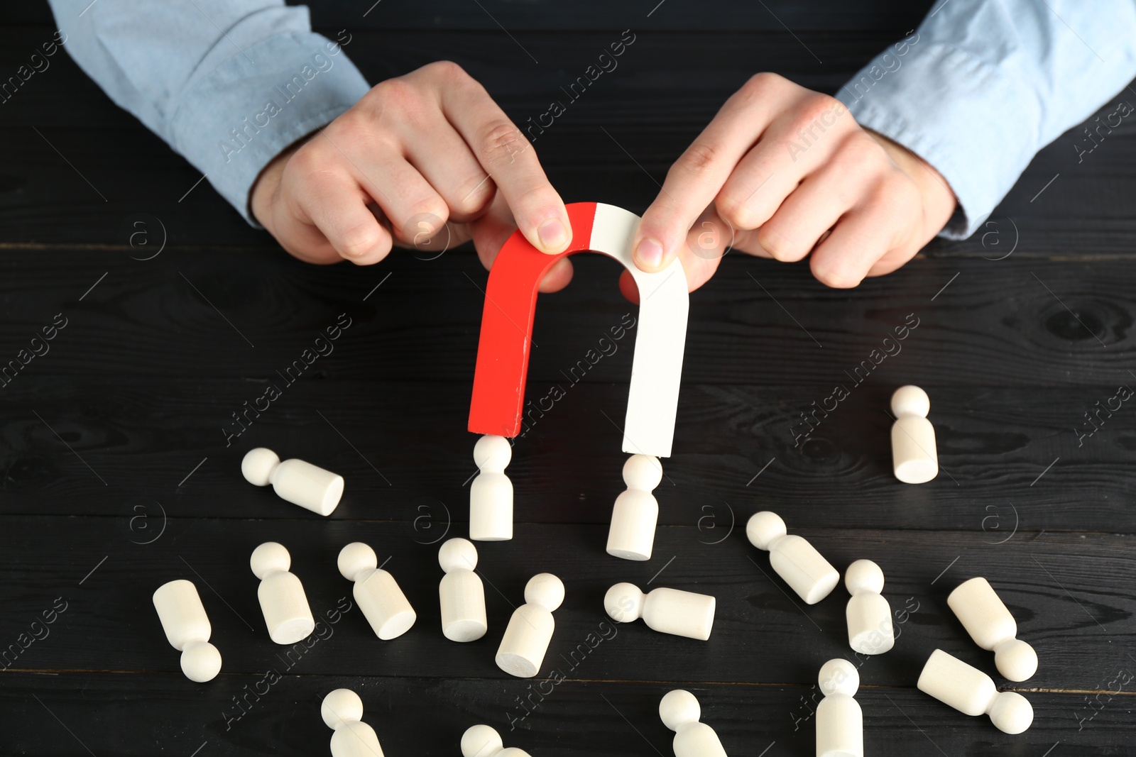 Photo of Man with magnet attracting human figures at black wooden table, closeup