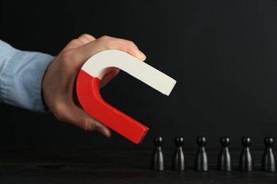 Photo of Man with magnet attracting black pieces at wooden table, closeup