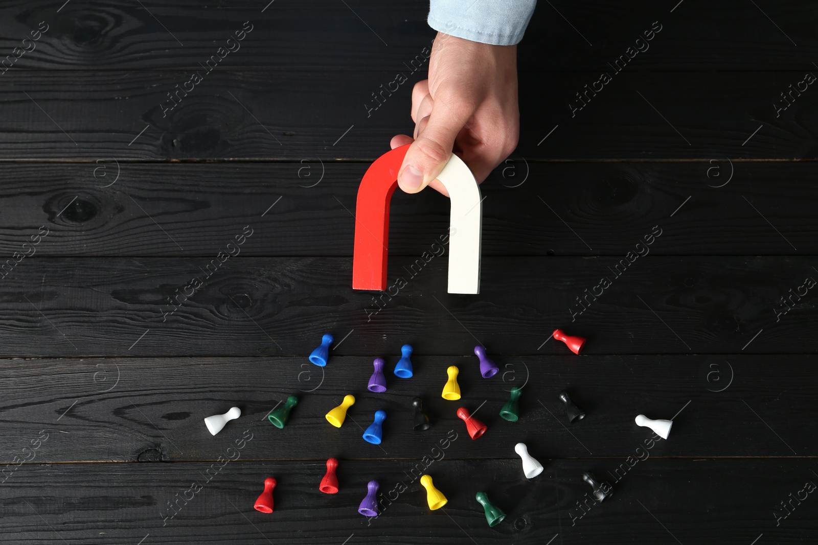 Photo of Man with magnet attracting different colorful game pieces at black wooden table, above view