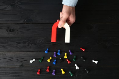 Photo of Man with magnet attracting different colorful game pieces at black wooden table, above view