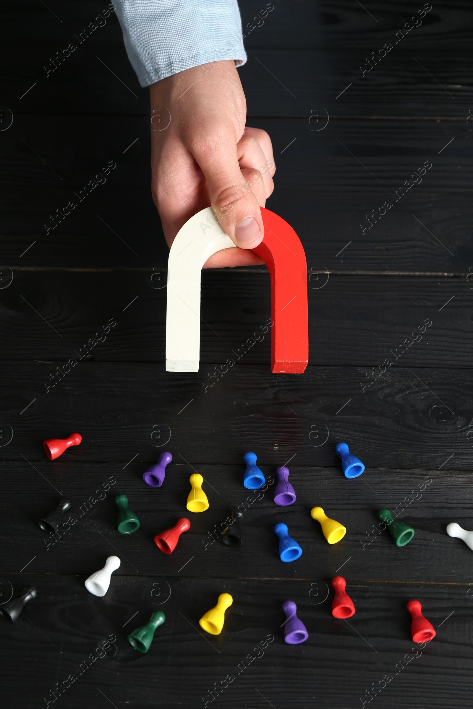 Photo of Man with magnet attracting different colorful game pieces at black wooden table, closeup