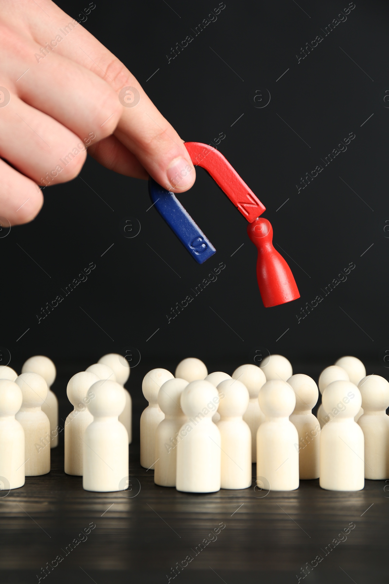 Photo of Man with magnet attracting red piece among wooden ones at black table, closeup