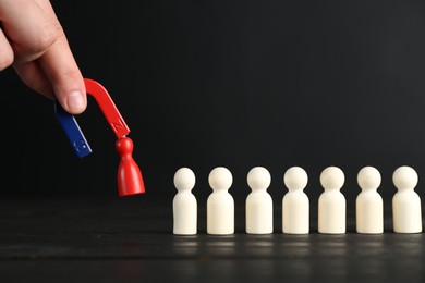 Photo of Man with magnet attracting red piece among wooden ones at black table, closeup