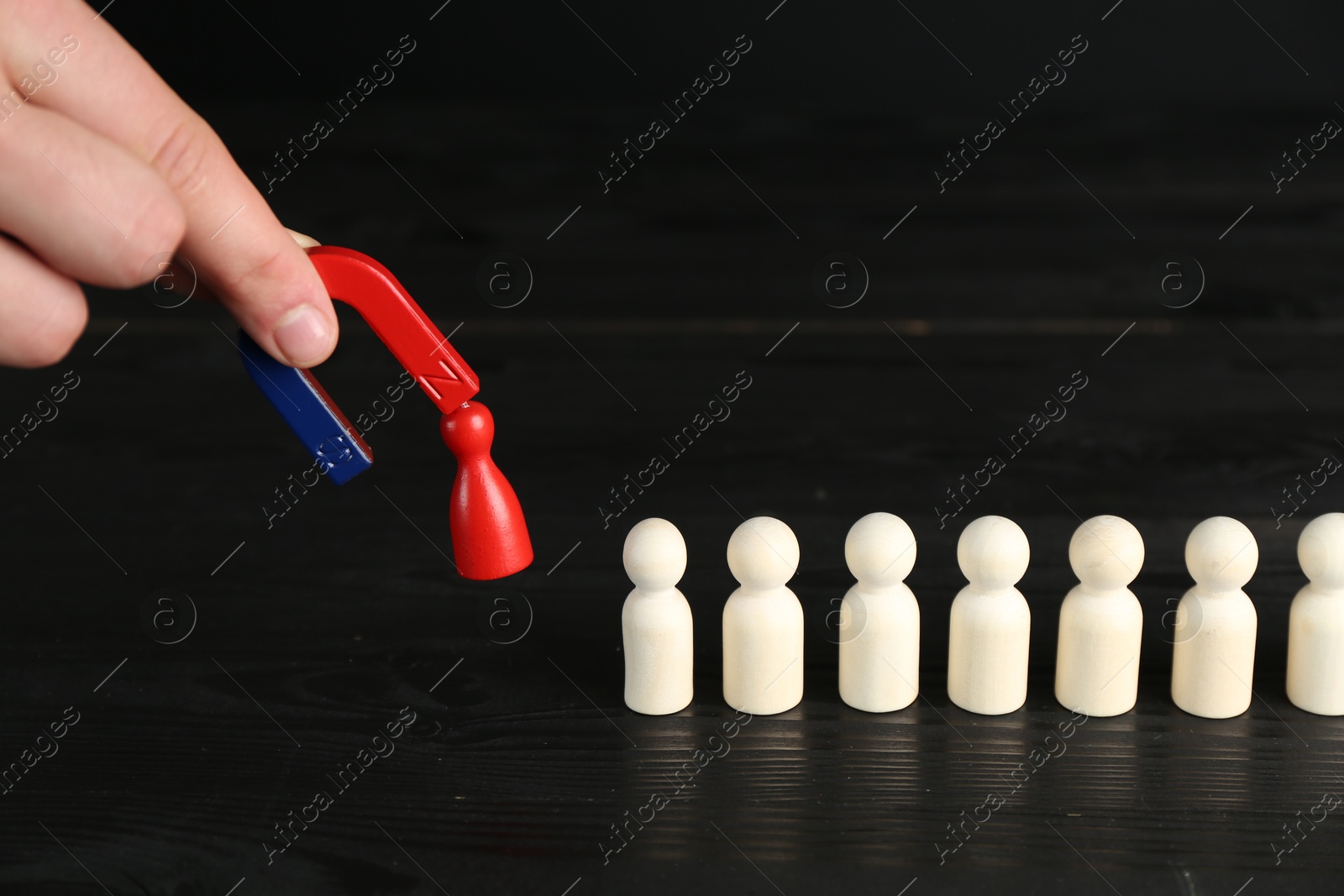 Photo of Man with magnet attracting red piece among wooden ones at black table, closeup