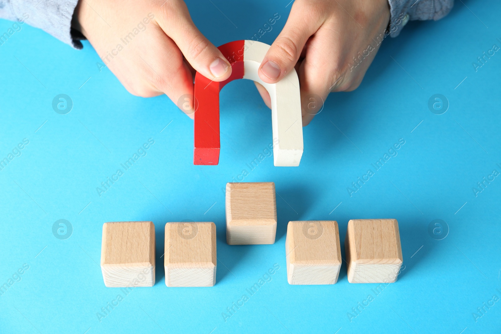 Photo of Man with magnet attracting wooden cubes on light blue background, closeup