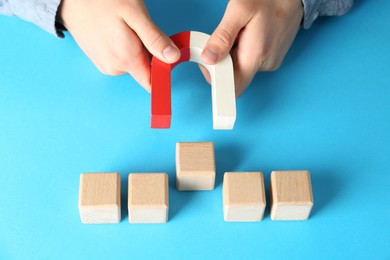 Photo of Man with magnet attracting wooden cubes on light blue background, closeup