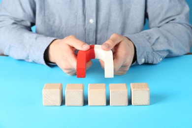 Photo of Man with magnet attracting wooden cubes on light blue background, closeup