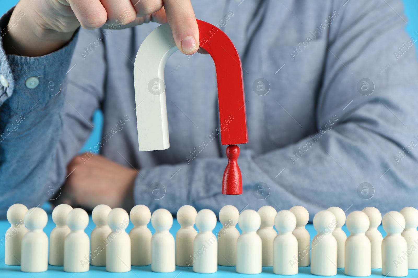 Photo of Man with magnet attracting red piece among wooden ones on light blue background, closeup