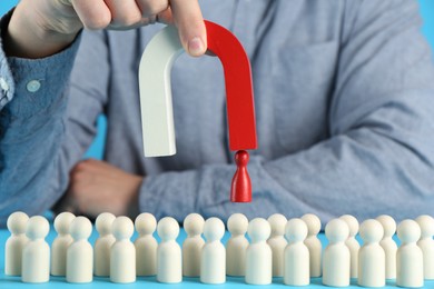 Photo of Man with magnet attracting red piece among wooden ones on light blue background, closeup