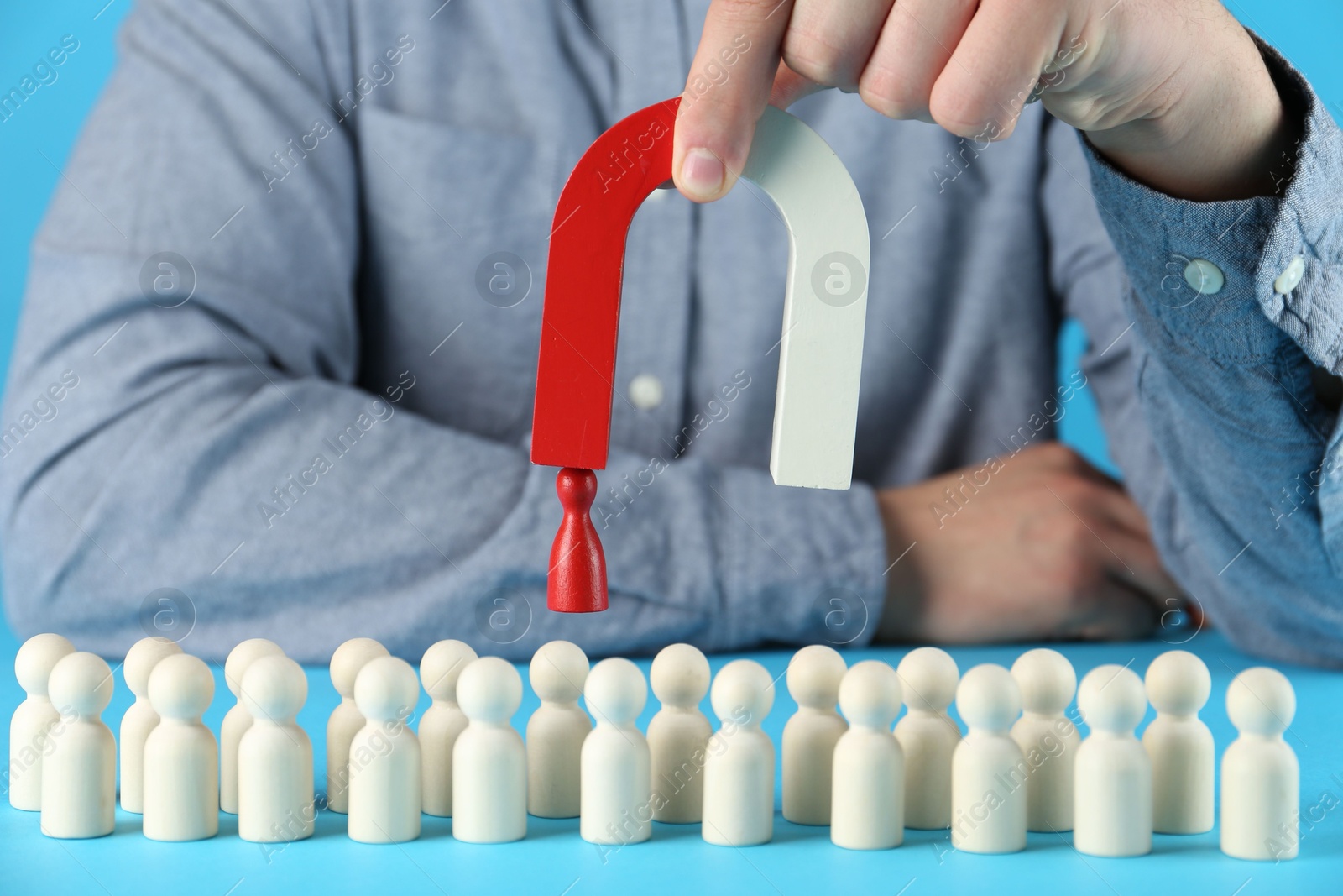 Photo of Man with magnet attracting red piece among wooden ones on light blue background, closeup